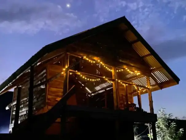 The wooden lodge lit with festoon lights after dark