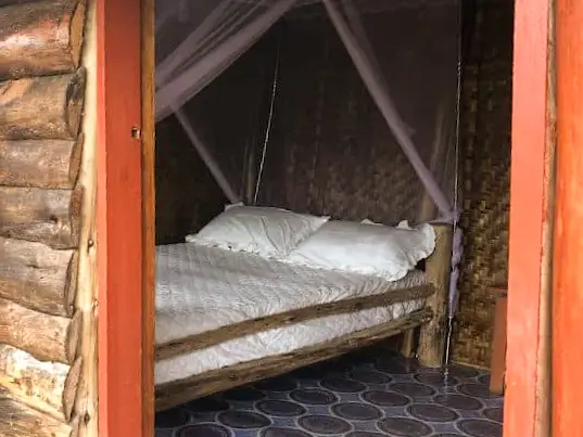A double bed under a mosquito net in a log-walled room