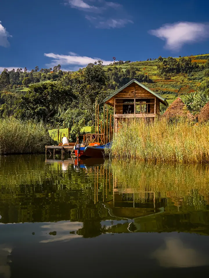 A wooden lakeside cabin with boats moored at a jetty, mirrored in the water