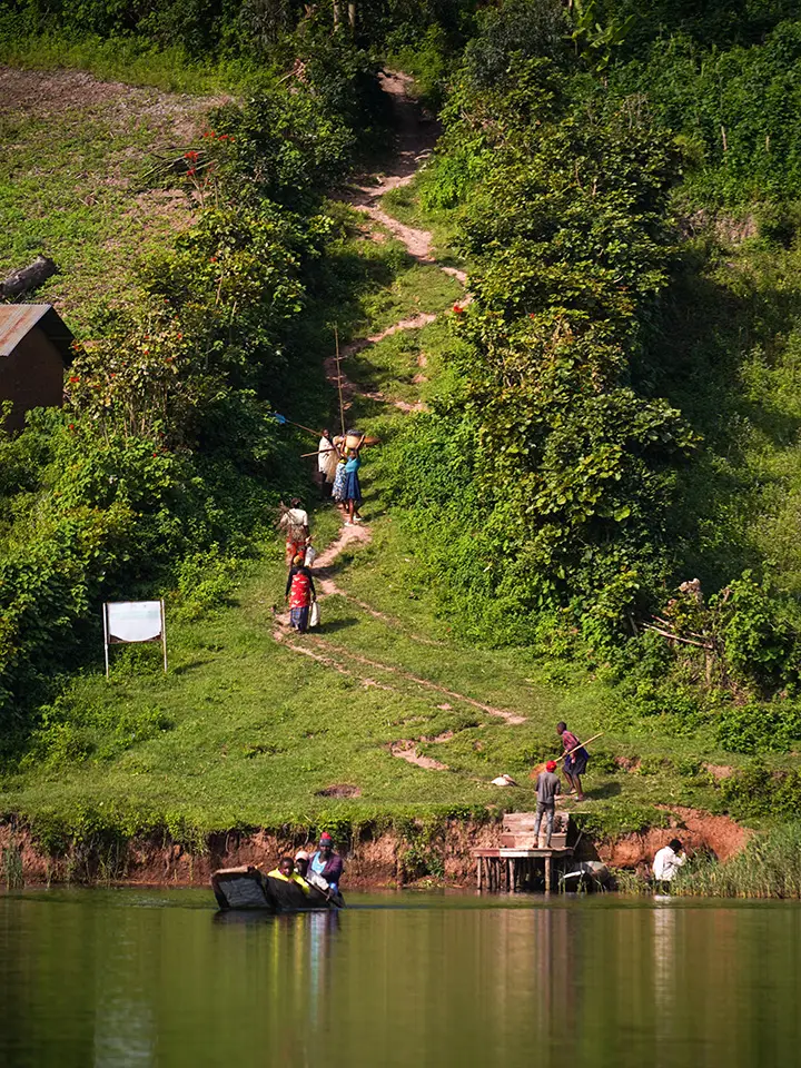 Villagers walking a footpath down the hillside to a canoe at the water's edge