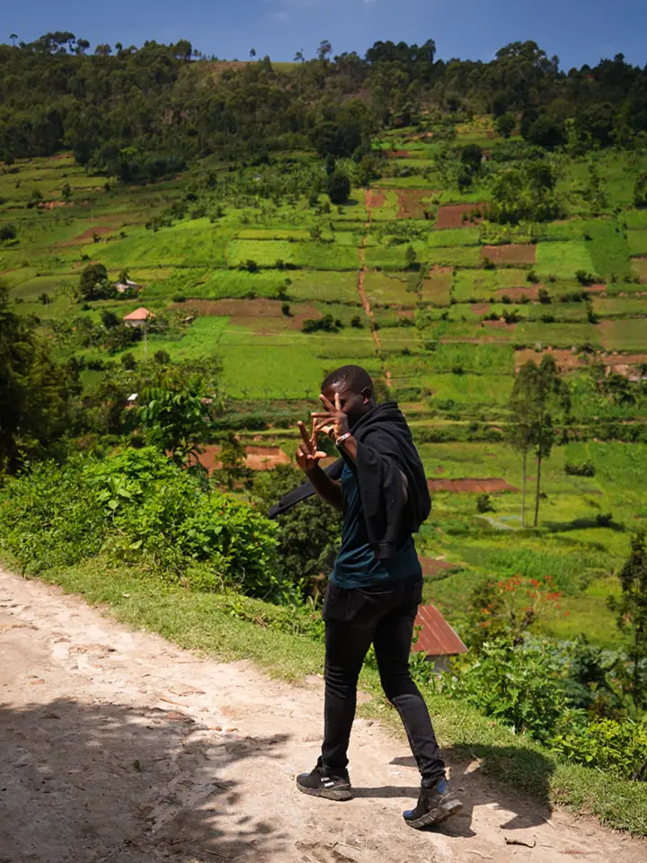 A young man on a dirt path above a valley of green terraced fields